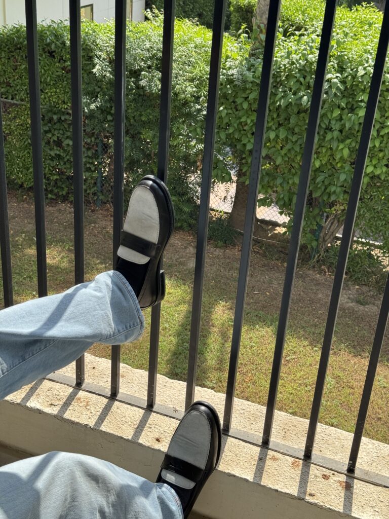 Penny Blue canvas loafers displayed in a hotel balcony setting